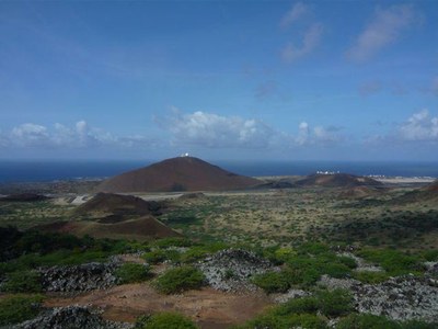 brown sandy hills with a green fertile plateau surrounding them and the sea behind