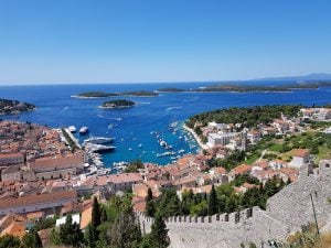 the town of hvar descends down the hillside from the castle to the harbor which is square and lined with all sizes of boats - in the distance are a litter of small islands