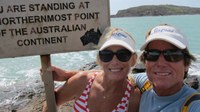 couple both wearing sunglasses and white caps smiling at the camera holding on to the sign at the top of australia