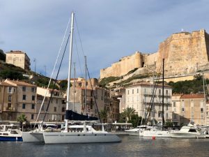 tall pretty buildings in front of a castle around a harbour with yachts berthed