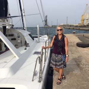 a white catamaran alongside a concrete dock with a lady in a black short skirt and black sleeveless top standing next to it.