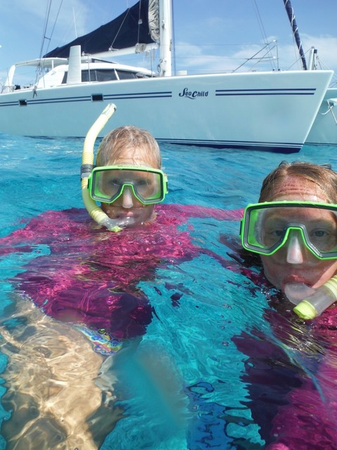 two women in pink wetsuits and green snorkels on the surface facing the camera next to a white boat in blue water