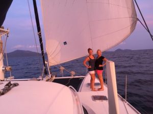 pink glow over the whole photo with a mum and daughter standing on the foredeck of the boat with the big foresail up