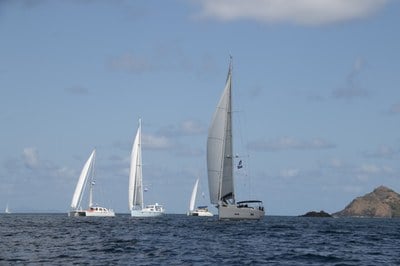 Several rally yachts running on a broad reach with mainsail and jib under a blue sky in the Caribbean