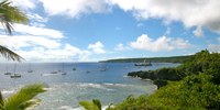 coastline with trees and offshore reef with yachts tied to mooring balls and a blue cloudy sky