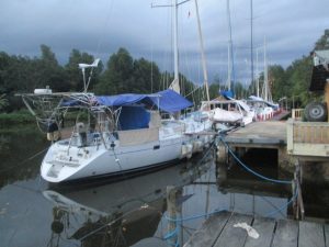 wooden high dock with several boats alongside with muted grey sky, narrow river and trees and very calm still water