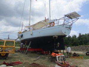 a white yacht with a black keel and deck awning propped up with wooden poles on a flat piece of dirt/grass