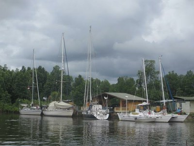 a number of yachts moored alongside a wooden pontoon with a club house behind, a forest and stormy skies
