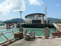 railings on a pier with a trolley parked next to them - blue water behind and the other side of the water a round building with glass and a flat roof