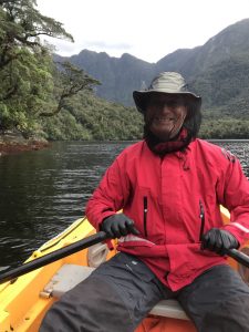 View of man paddling kayak with a bug net over his head in the Fiordlands, South Island, New Zealand