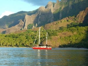 Yacht migration with her red hull lies quietly at anchor in the Marquesas with a spectacular mountainous backdrop
