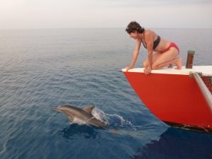A dolphin jumps out of the water in front of the bow of yacht Migration and Alene is just a few feet away onboard the boat