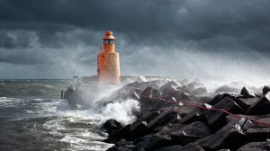 orange lighthouse surrounded by rocks in stormy weather