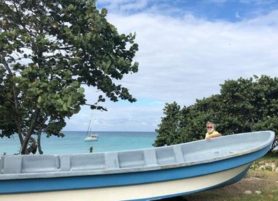 author brian simm next to a local pirogue on the beach with his boat at anchor behind