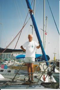 Jim on board his boat standing on the bow holding onto the furled headsail
