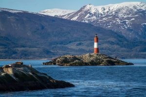 A lighthouse on a rocky outcrop with snow topped mountains behind