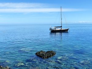 yacht at anchor in crystal clear water with a reef in the foreground and a rock shaped like a heart