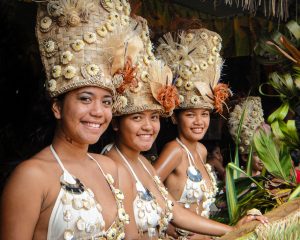 three smiling local girls dressed in national dress with reed headresses decorated with shells and white bikinis decorated with shells