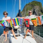 lisa and captain fabio standing on the deck of the boat holding the courtesy flags of all the countries they have sailed to