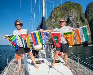 lisa and captain fabio standing on the deck of the boat holding the courtesy flags of all the countries they have sailed to