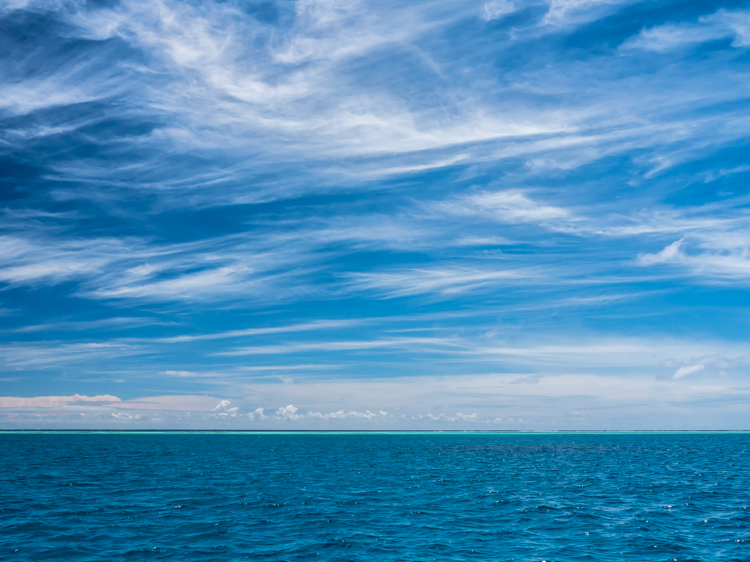 blue water and blue sky with light wispy clouds in the maldives