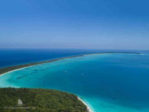 a sheltered anchorage inside a long arm of land with bright blue water, white sand and 2 yachts at anchor