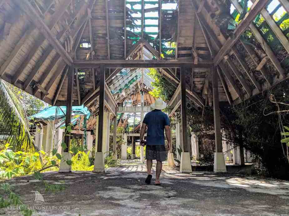 a man walking through the skeleton of a building with wooden rafters, slowly crumbling away