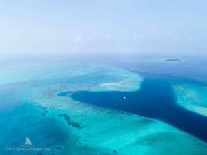 aerial view of a reef pass and protected anchorage with two yachts anchored in deep blue water surrounded by light turquoise water