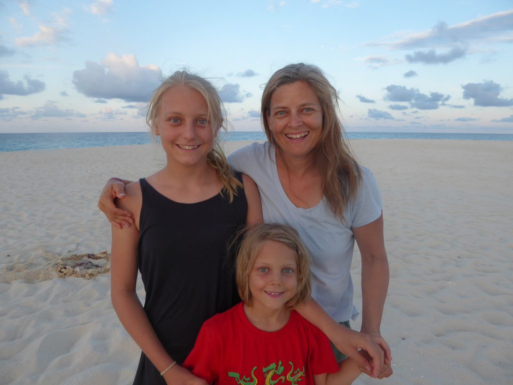 Mum melissa with her arm around her eldest daughter and co-author Reminy and youngest daugher standing in front on a beach in australia