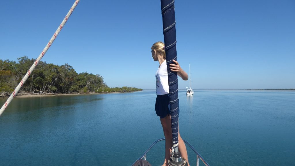 young teenage girl with blond hair and wearing shorts and a t shirt balanced on the bow of the boat looking out to sea