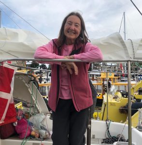 Jeanne leaning on the rail of her boat dressed in a pink long sleeved top and pink body warmer and smiling