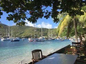 view from a beach side restaurant across the table under a shady tree to the bay with boats anchored beyond