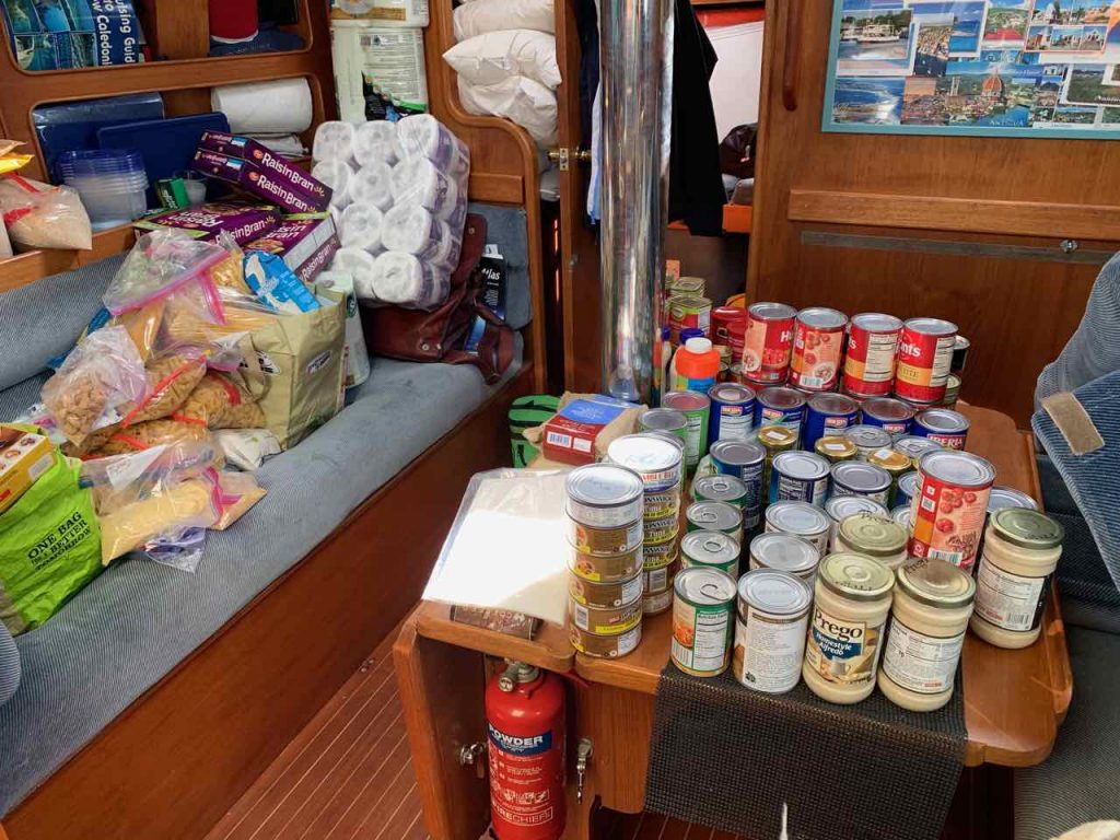 interior of the boat with cans of tinned fish, meat, vegetables, toilet rolls, all piled up on the bunks and table and floor