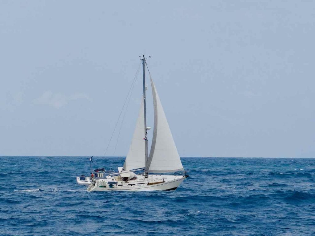 white boat with full sail up, also white, and many solar panels attached to it, sailing in a blue sea