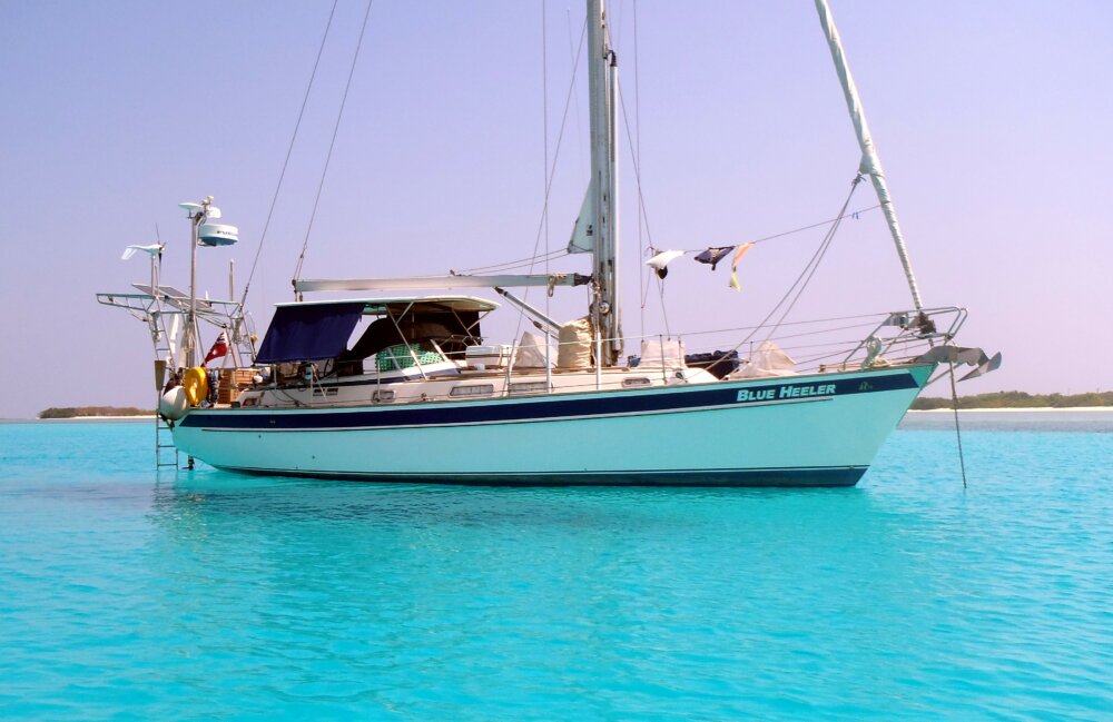 yacht at anchor with an awning over the cockpit to keep the boat cool floating on irredesent blue water