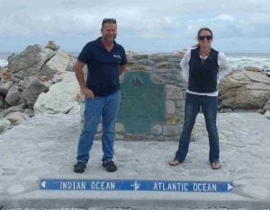 a man and woman in jeans standing on a concrete marker that shows the division between 2 oceans