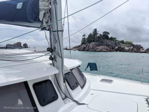 Looking over the deck of a catamaran with a rocky islet beyond topped with trees
