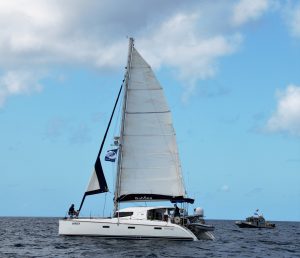 catamaran that suffered the mast failure in this story with main up and starting to roll out the foresail at the start line of the event with a small boat behind probably the committee boat