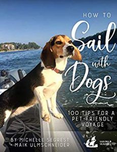 A beagle on deck on a boat at sea with his ears flapping in the wind and land way behind