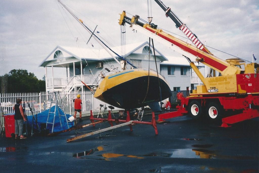 a crane lifting upright a yacht in a boatyard that has fallen sideways onto some railings and a house