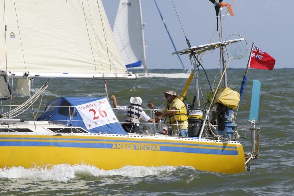 yellow hulled boat with a white sail and racing number and a man in a yellow shirt at the helm