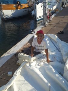 a smiling lady in a white t shirt with a red cap sitting on a large white sail on a pontoon making repairs