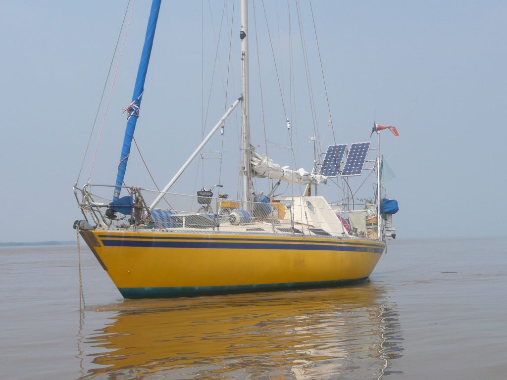 a yacht at anchor in tranquil waters, bright yellow hull and white topsides with solar panels and large white doghouse