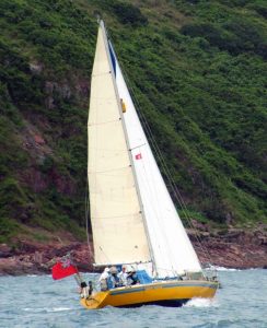 a yellow hulled white sail sailing boat heeled over and sailing along the coast