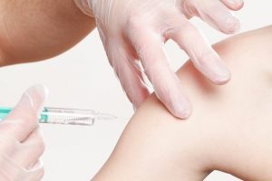 child's arm and a surgical gloved hand holding it with a syringe close by ready to vaccinate