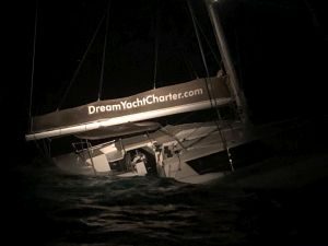 a catamaran sinking with most of the deck submerged and just the topsides and boom and mast sticking out of the water at night