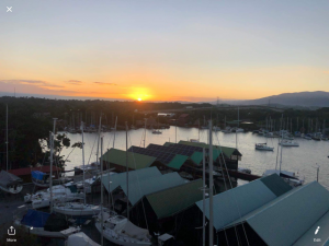 sunset over the river with a high arched bridge in the distance and marina buildings and boats at anchor in the foreground