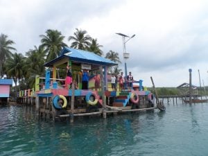 end of a jetty with brightly coloured tyres and a pagoda with a blue roof plus local smiling and waving goodbye