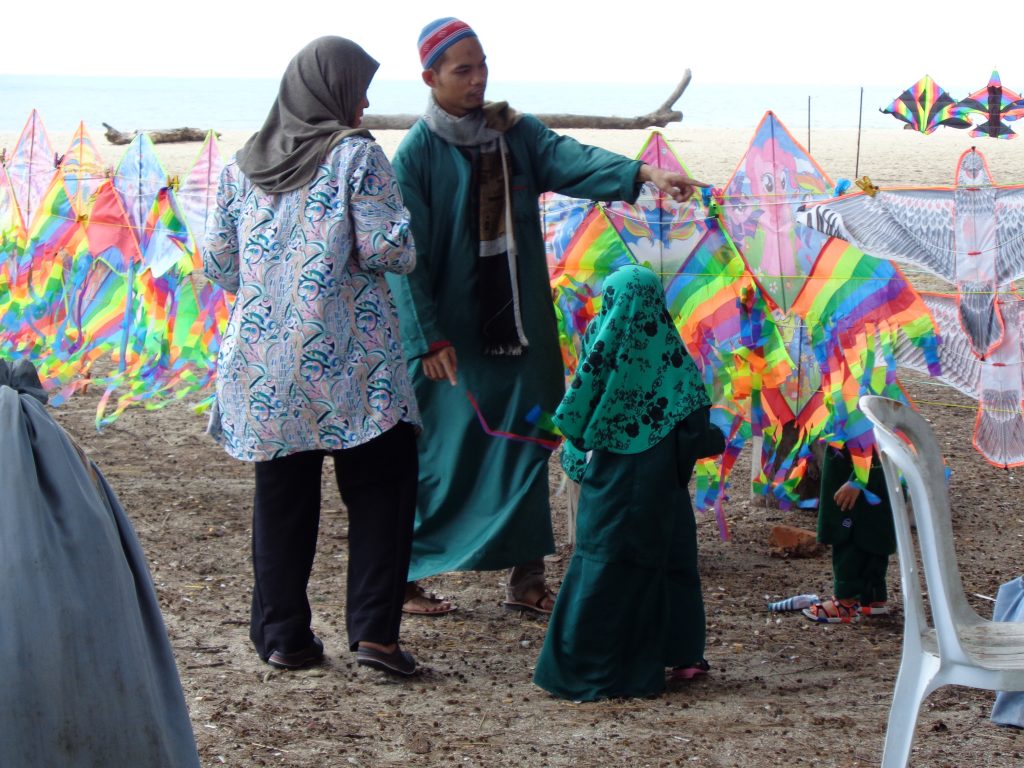 locals dressed in headscarves and long caftans with brightly coloured kites on the beach