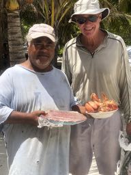 two men - the one on the left shorter and heavier, the one on the right taller and thinner both wearing hats and cover up shirts and holding bowls of food